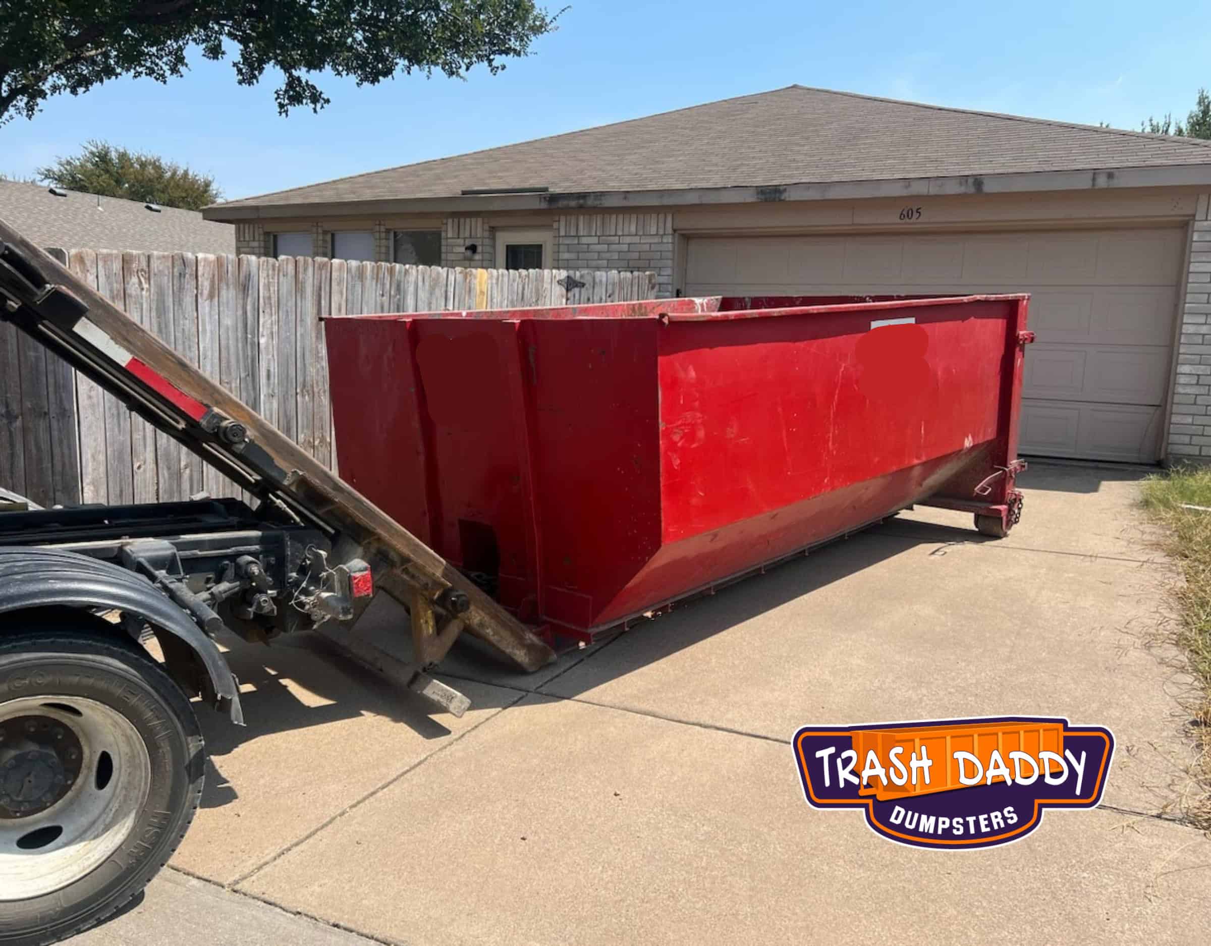 red 20 yard dumpster being delivered in a residential driveway