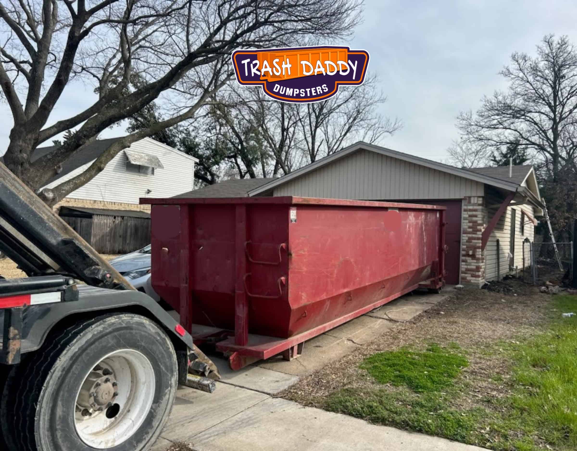 red 30 yard dumpster being delivered in a residential driveway